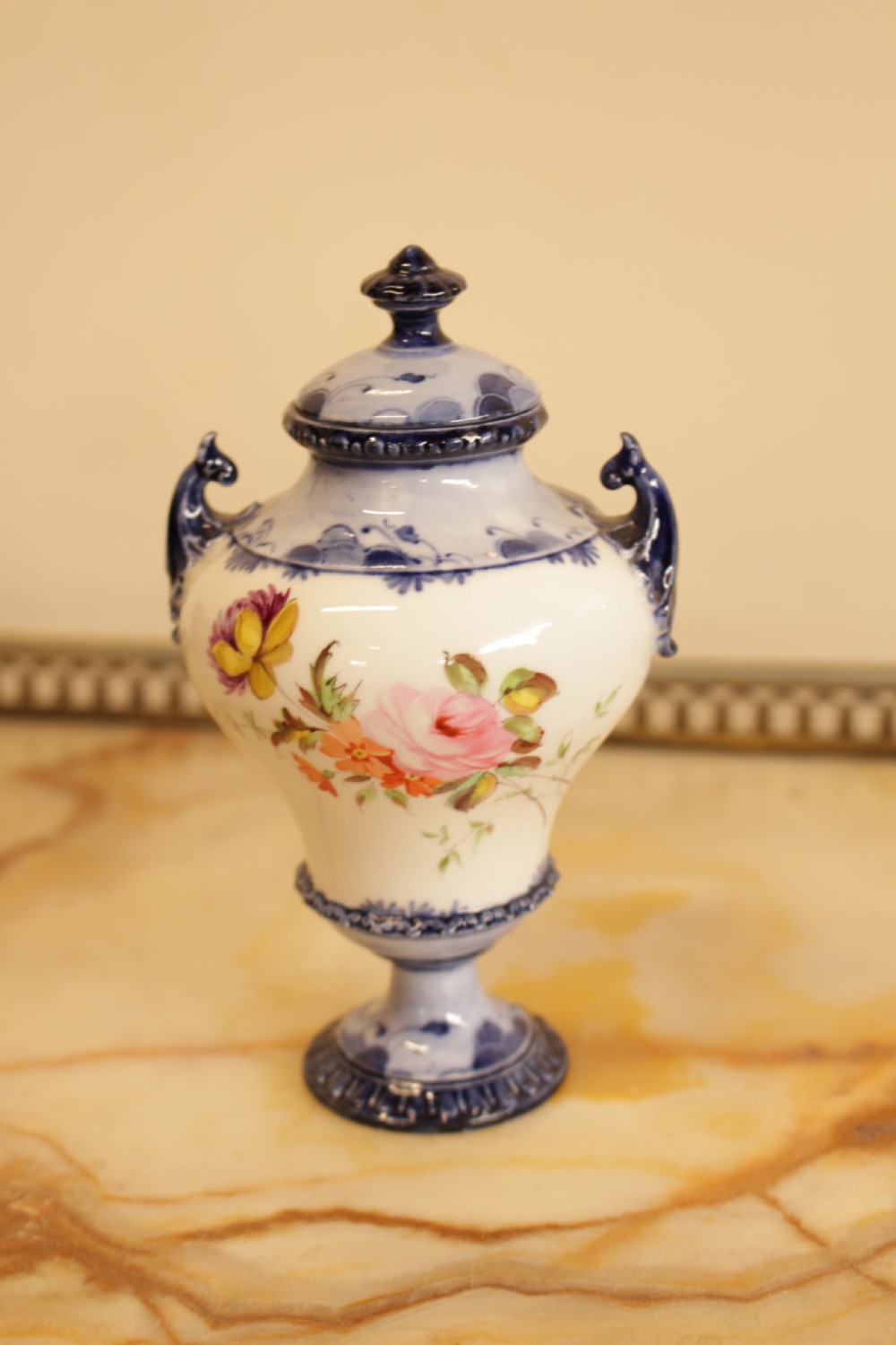 An antique porcelain lidded urn featuring hand-painted floral motifs, cobalt blue handles, and a pedestal base. View II