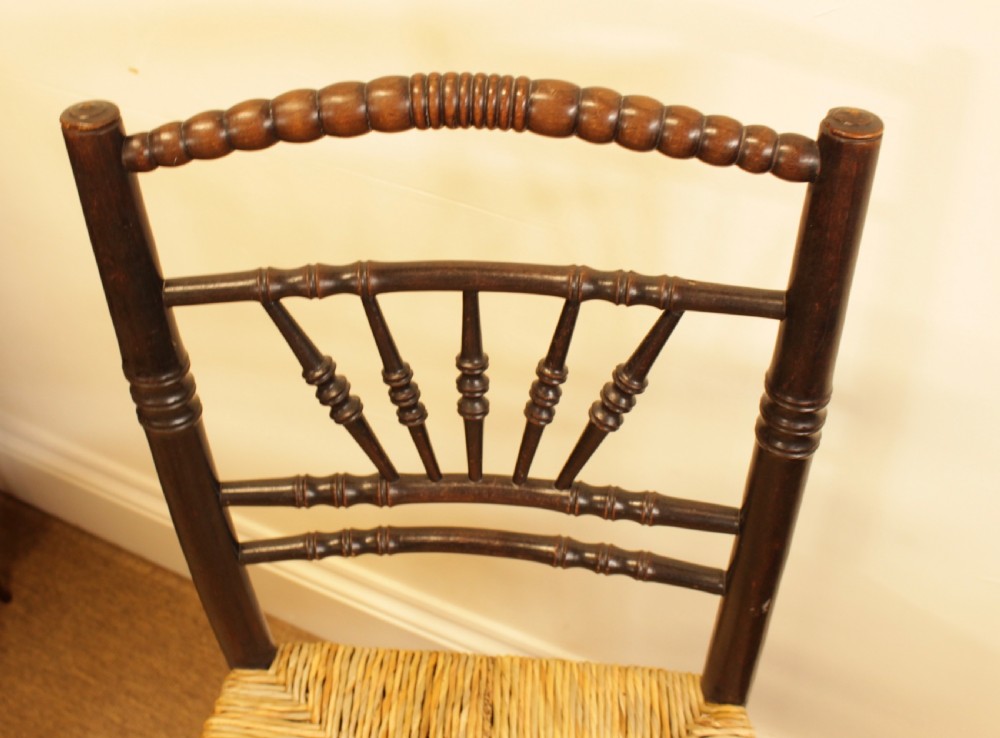 A dark stained wooden side chair featuring a fan-shaped spindle back, turned stretchers, and a woven rush seat. View V