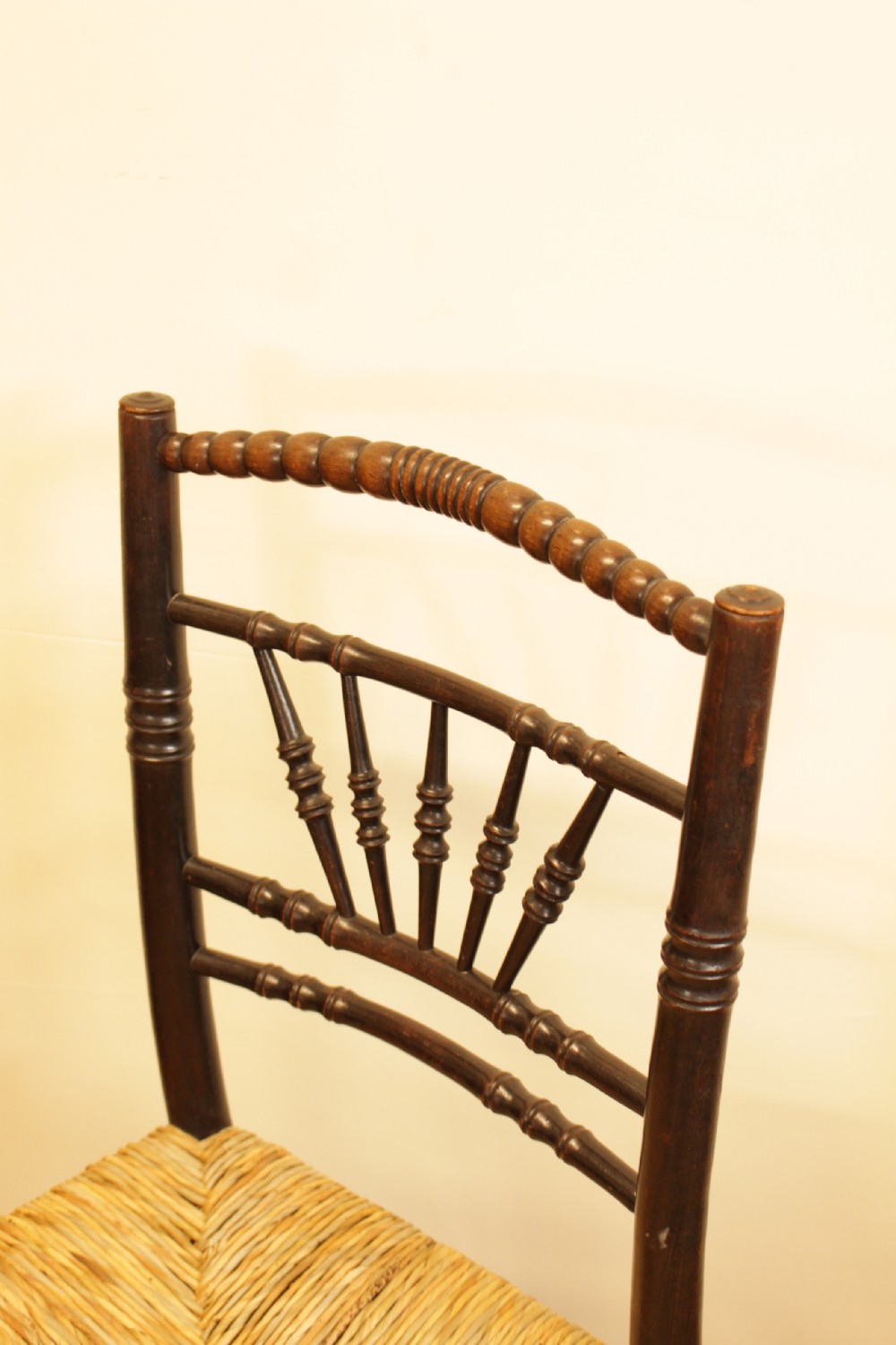 A dark stained wooden side chair featuring a fan-shaped spindle back, turned stretchers, and a woven rush seat. View VI