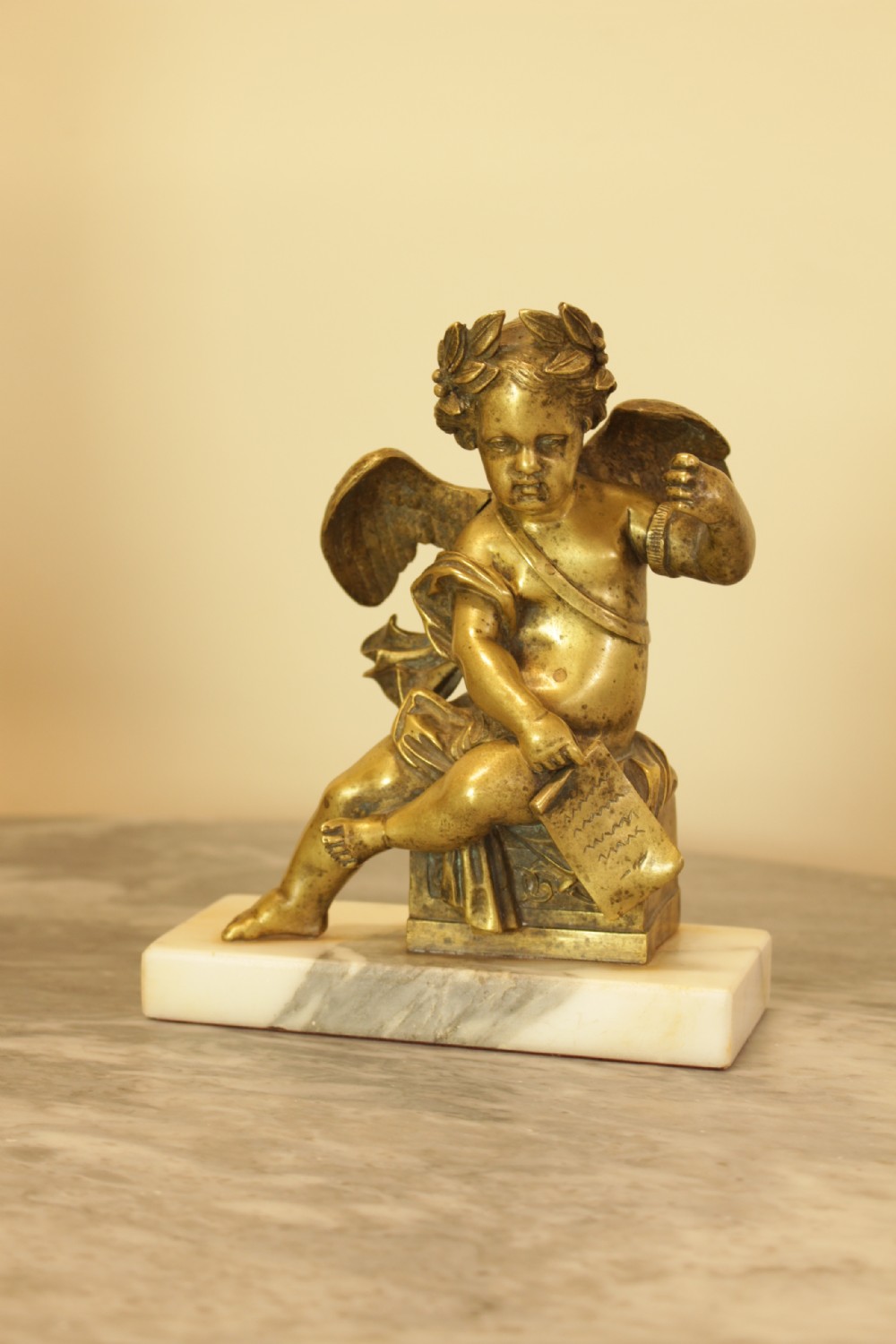 A 19th-century French gilt bronze sculpture of a winged putto wearing a laurel wreath and holding a scroll, mounted on a rectangular veined marble base.