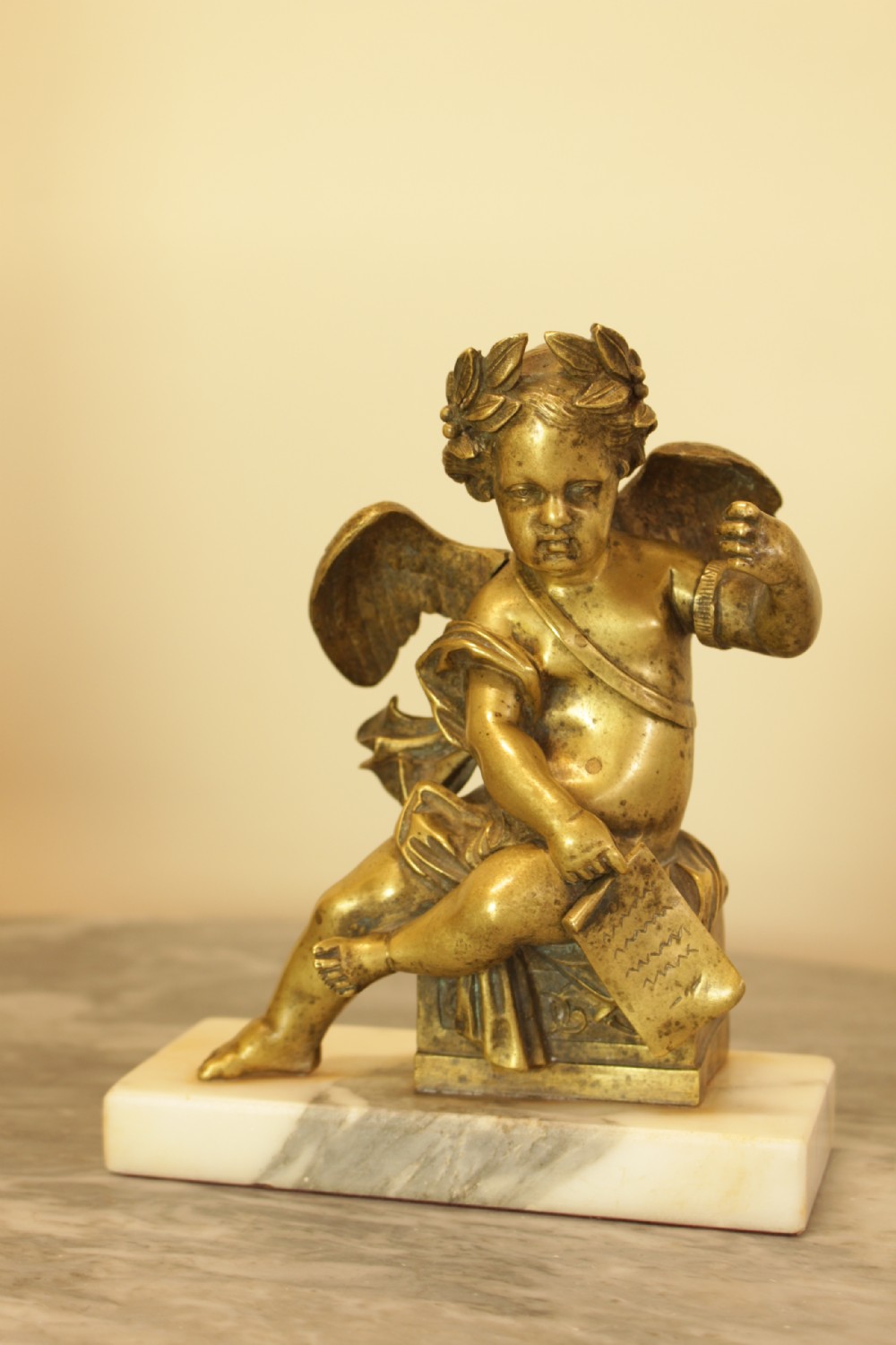 A 19th-century French gilt bronze sculpture of a winged putto wearing a laurel wreath and holding a scroll, mounted on a rectangular veined marble base. View II