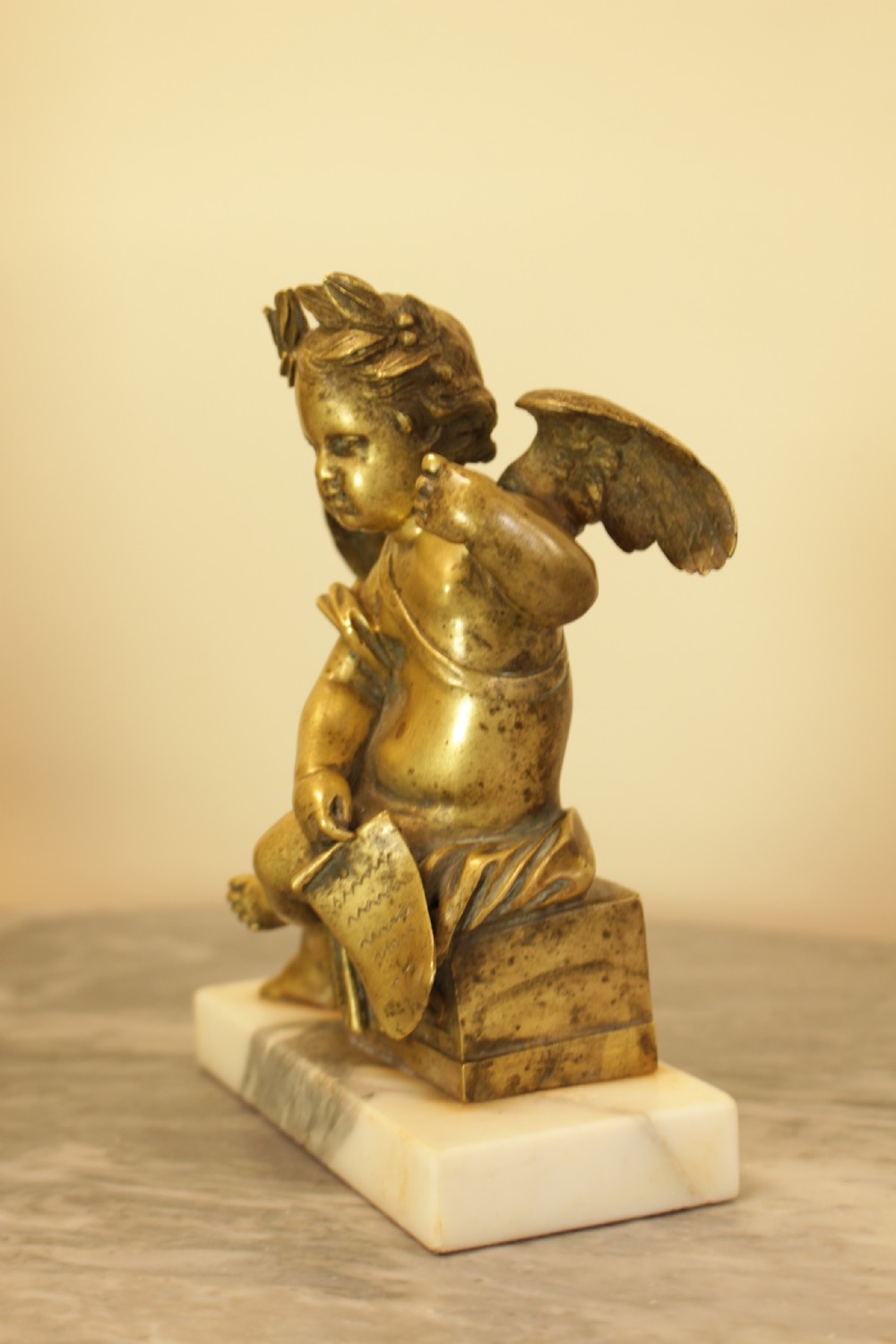 A 19th-century French gilt bronze sculpture of a winged putto wearing a laurel wreath and holding a scroll, mounted on a rectangular veined marble base. View III