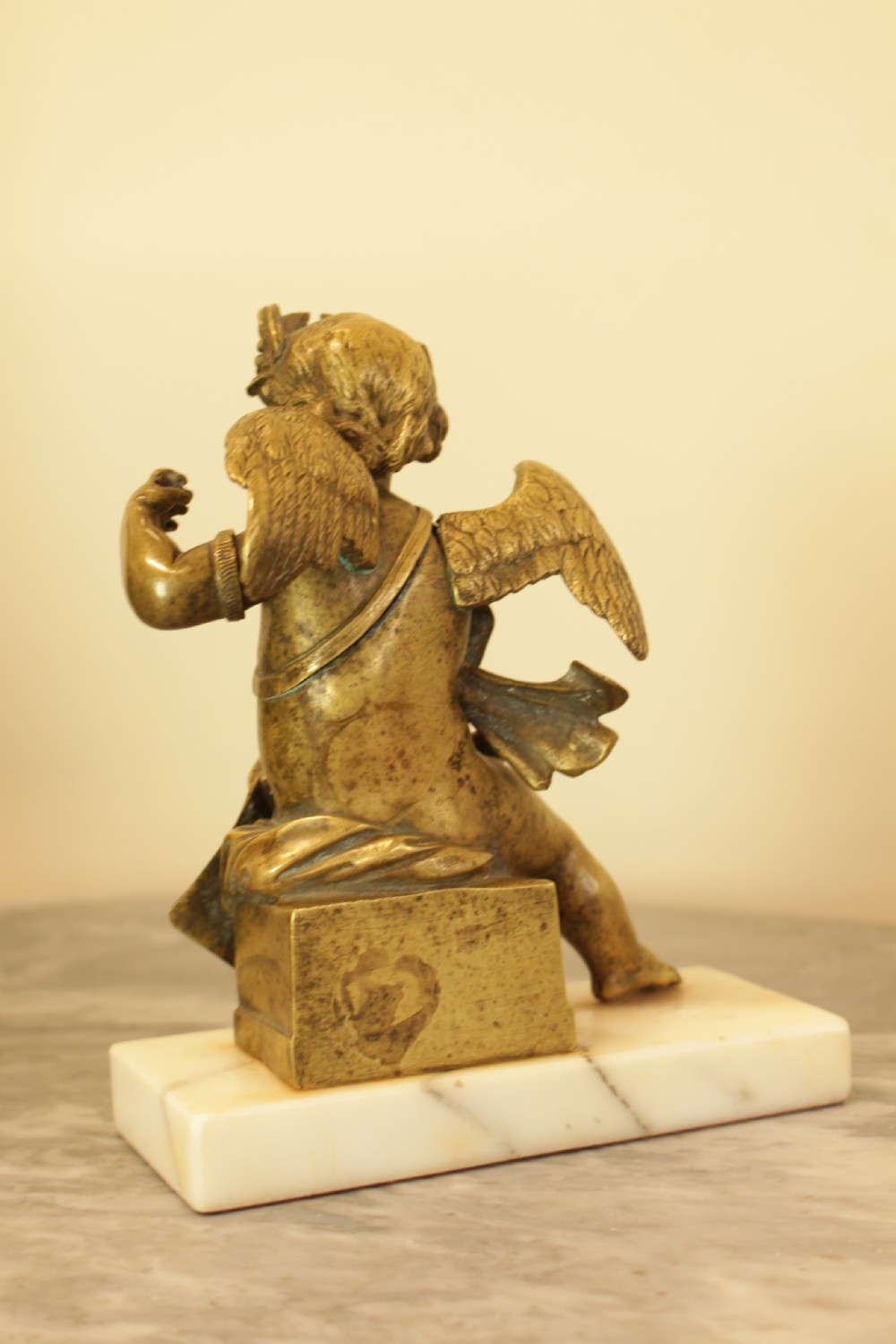 A 19th-century French gilt bronze sculpture of a winged putto wearing a laurel wreath and holding a scroll, mounted on a rectangular veined marble base. View IV