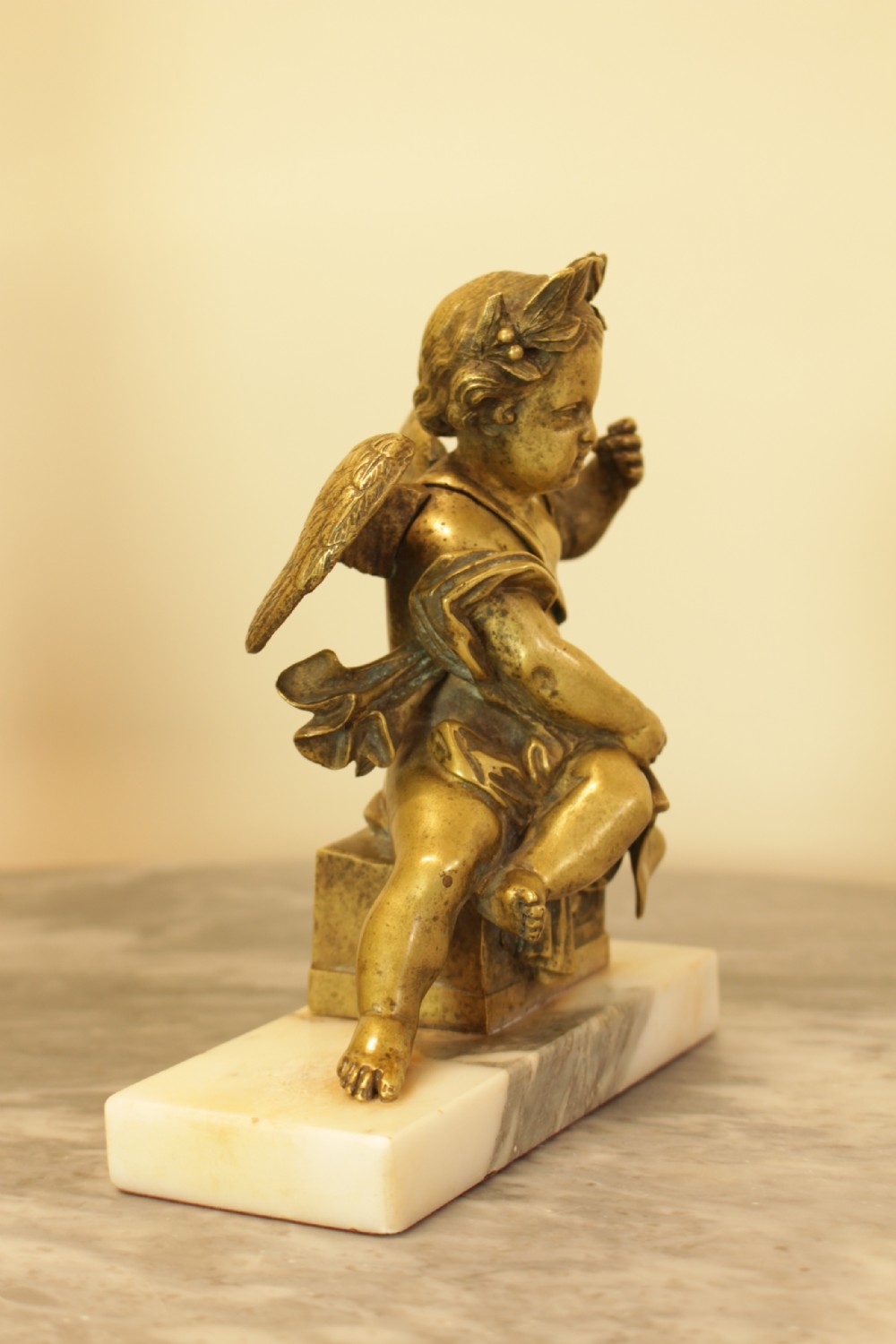 A 19th-century French gilt bronze sculpture of a winged putto wearing a laurel wreath and holding a scroll, mounted on a rectangular veined marble base. View VI