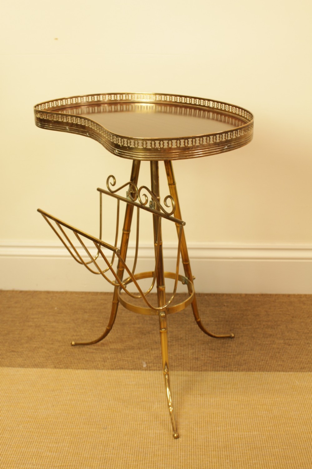 A brass occasional side table featuring a kidney-shaped top surface with a pierced gallery rail, faux bamboo tripod legs, and an integrated wire magazine rack.