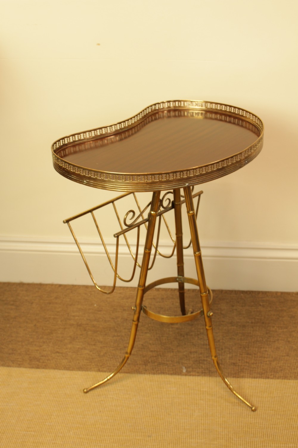 A brass occasional side table featuring a kidney-shaped top surface with a pierced gallery rail, faux bamboo tripod legs, and an integrated wire magazine rack. View VI