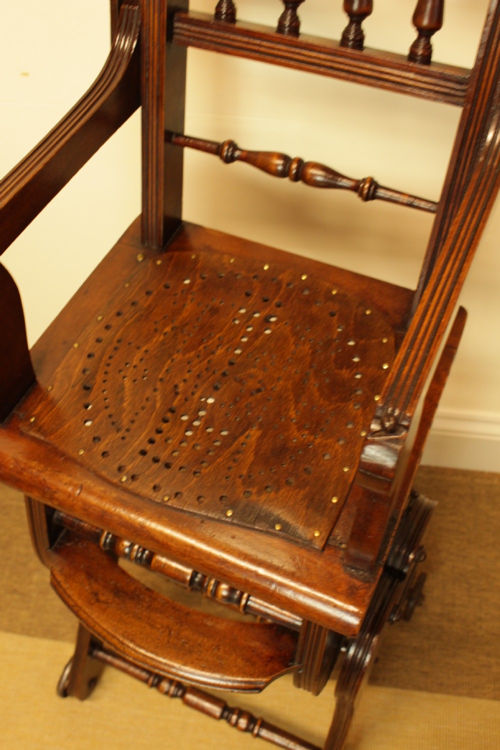 A Victorian dark brown beech metamorphic childs high chair featuring turned spindles, a perforated seat, and small wooden wheels. View VI