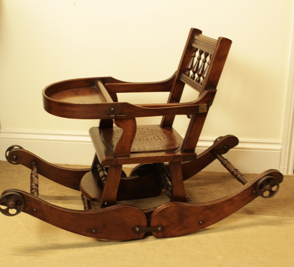 A Victorian dark brown beech metamorphic childs high chair featuring turned spindles, a perforated seat, and small wooden wheels. View IX