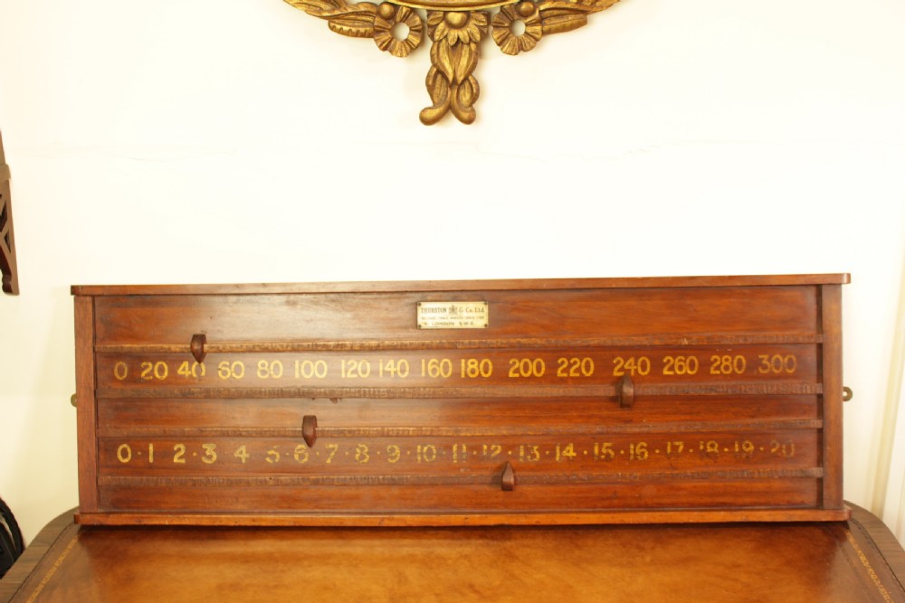 A rectangular mahogany billiards scoring board featuring two horizontal tracks with sliding wooden markers, yellow painted numbers, and a maker plaque at the top centre.