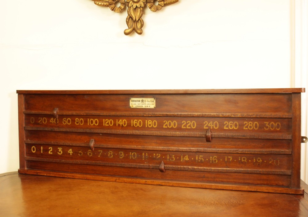 A rectangular mahogany billiards scoring board featuring two horizontal tracks with sliding wooden markers, yellow painted numbers, and a maker plaque at the top centre. View V