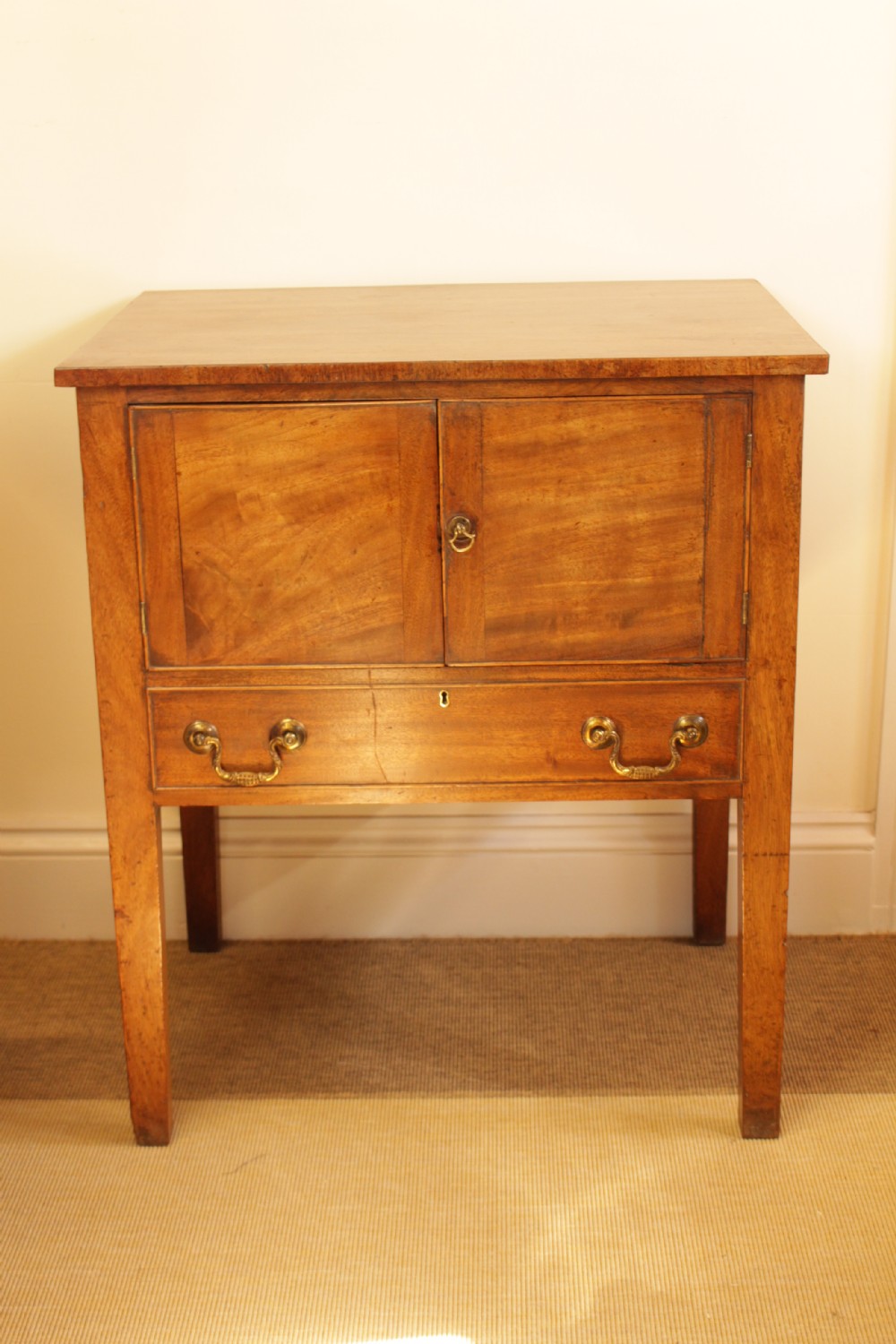 A Georgian mahogany cupboard featuring two panelled doors above a single drawer with brass swan-neck handles, supported on four straight square legs.