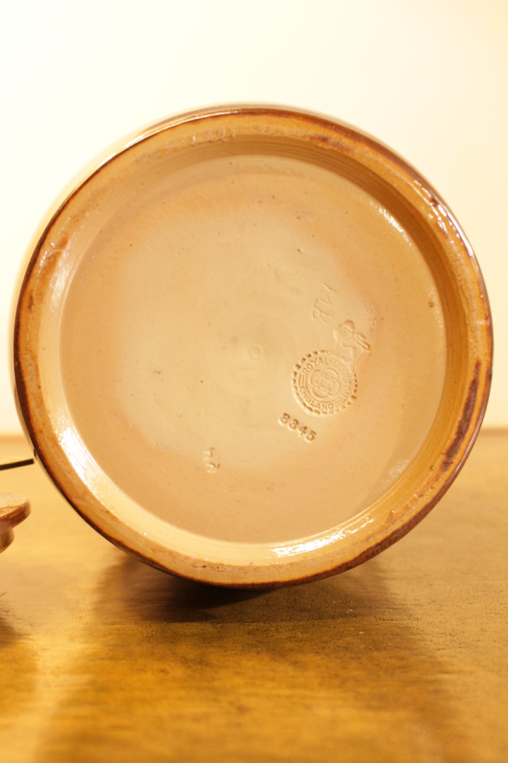 A cylindrical Royal Doulton stoneware tobacco jar decorated with a deep blue glaze, ochre stylized floral motifs, and a metal press-lid mechanism. View II
