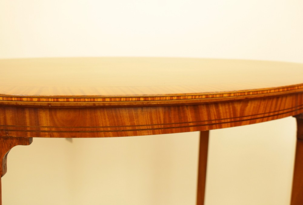 An antique oval satinwood occasional table featuring a crossbanded veneered top, slender tapered legs, and a matching lower undertier shelf. View IV