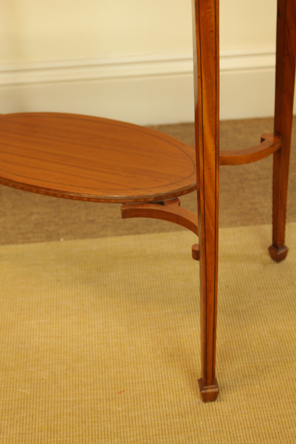 An antique oval satinwood occasional table featuring a crossbanded veneered top, slender tapered legs, and a matching lower undertier shelf. View V