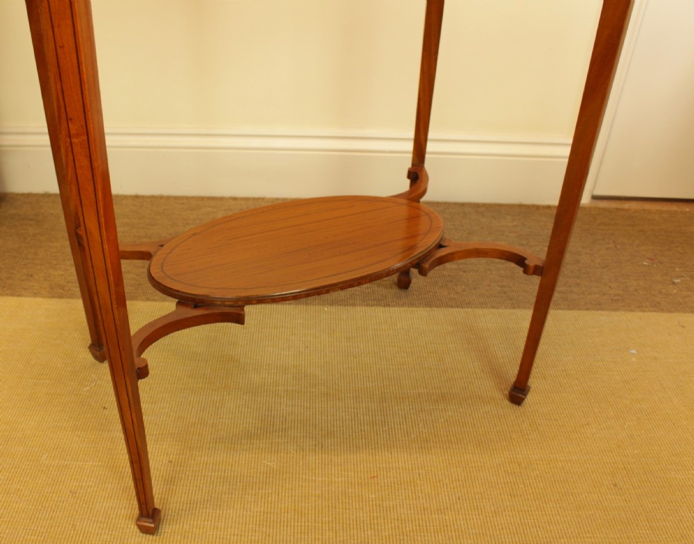 An antique oval satinwood occasional table featuring a crossbanded veneered top, slender tapered legs, and a matching lower undertier shelf. View VII