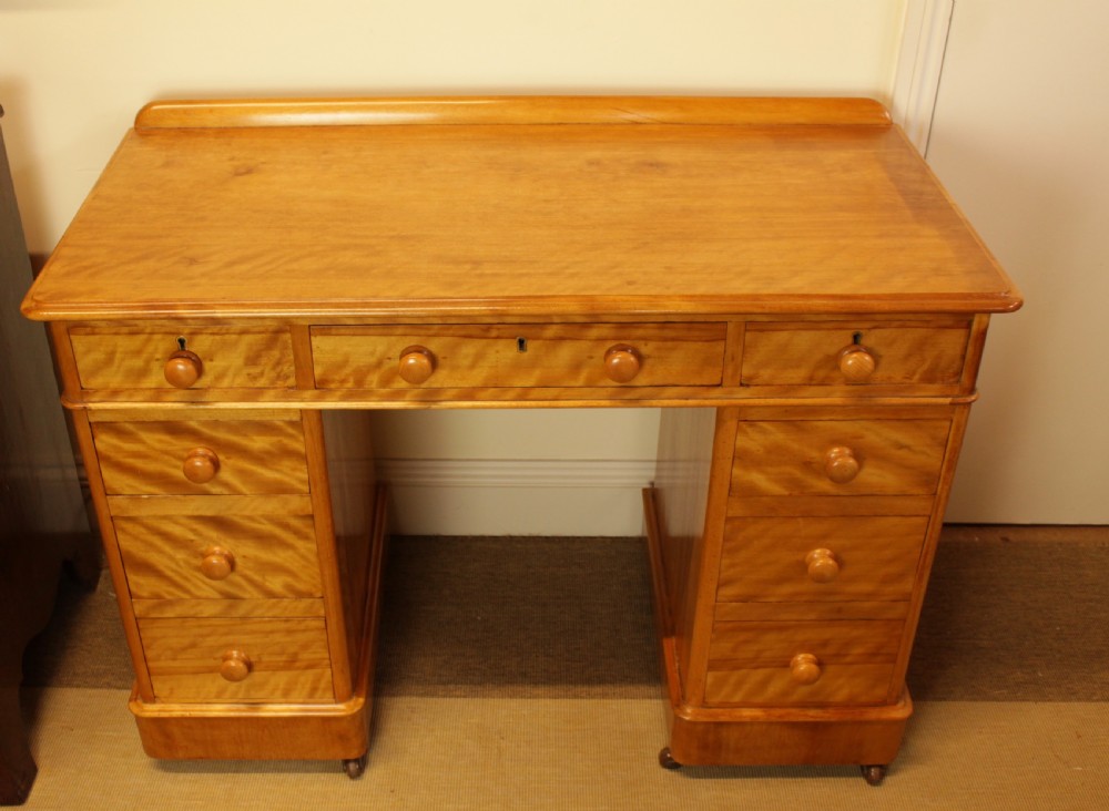 A late Victorian satin birch pedestal desk featuring nine drawers with turned handles, a low gallery back rail, and prominent golden wavy wood grain. View VI