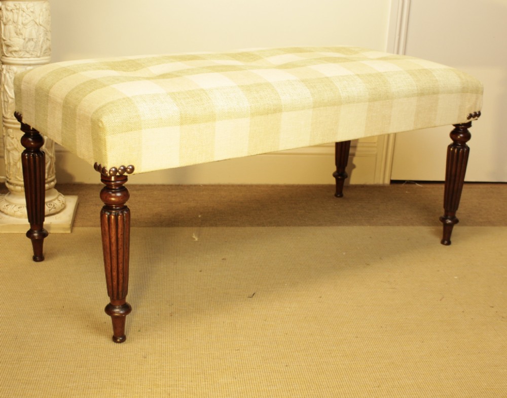 A late 19th-century mahogany stool featuring reeded turned legs, brass stud trim, and a checked cream upholstery top.