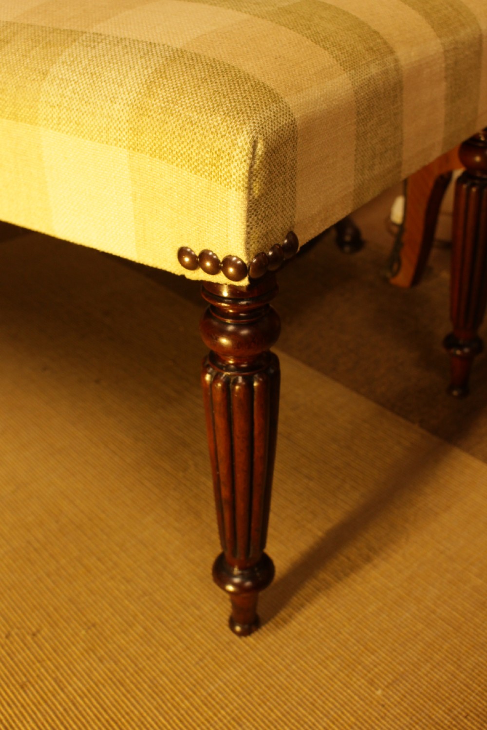 A late 19th-century mahogany stool featuring reeded turned legs, brass stud trim, and a checked cream upholstery top. View III