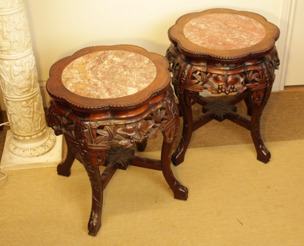 A pair of carved dark rosewood Chinese urn stands featuring lobed frames with inset circular rouge marble tops and intricate foliage aprons.
