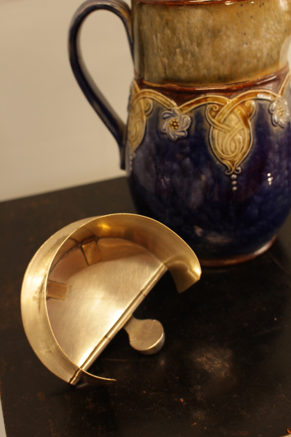 A Royal Doulton salt-glazed stoneware water jug featuring a cobalt blue body with raised relief scrollwork, an ochre neck, and a hinged metal lid. View VII