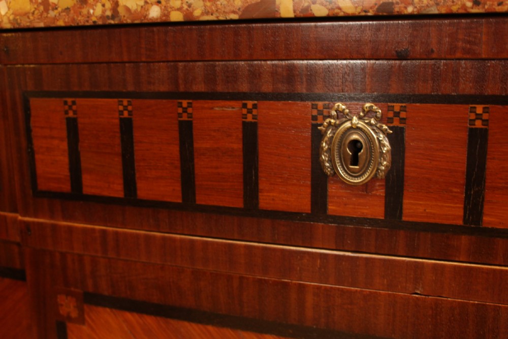 An early French Art Deco wooden commode featuring three drawer sections, geometric parquetry inlay, brass mounts, and a fitted marble top. View VI