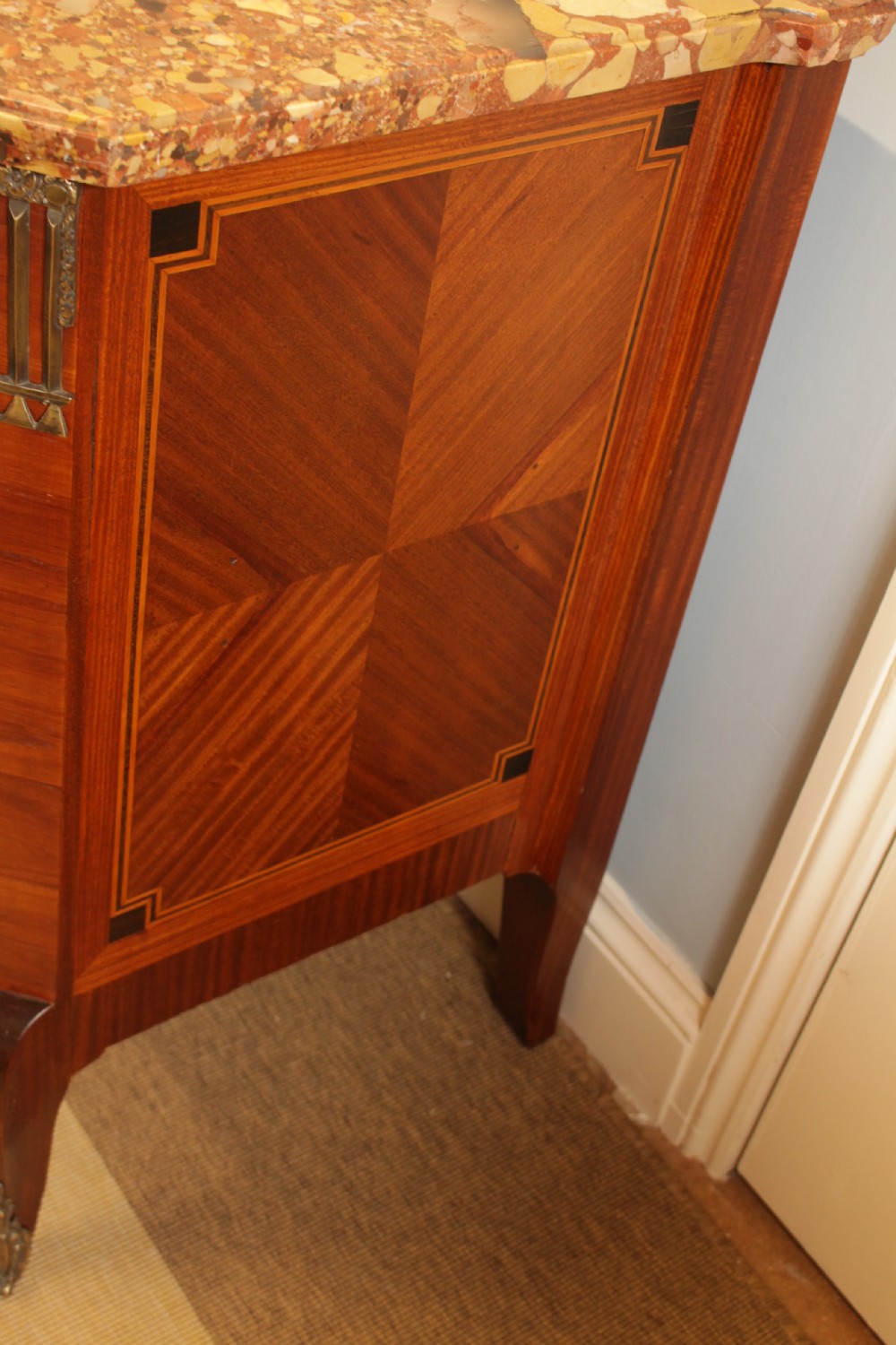 An early French Art Deco wooden commode featuring three drawer sections, geometric parquetry inlay, brass mounts, and a fitted marble top. View VII