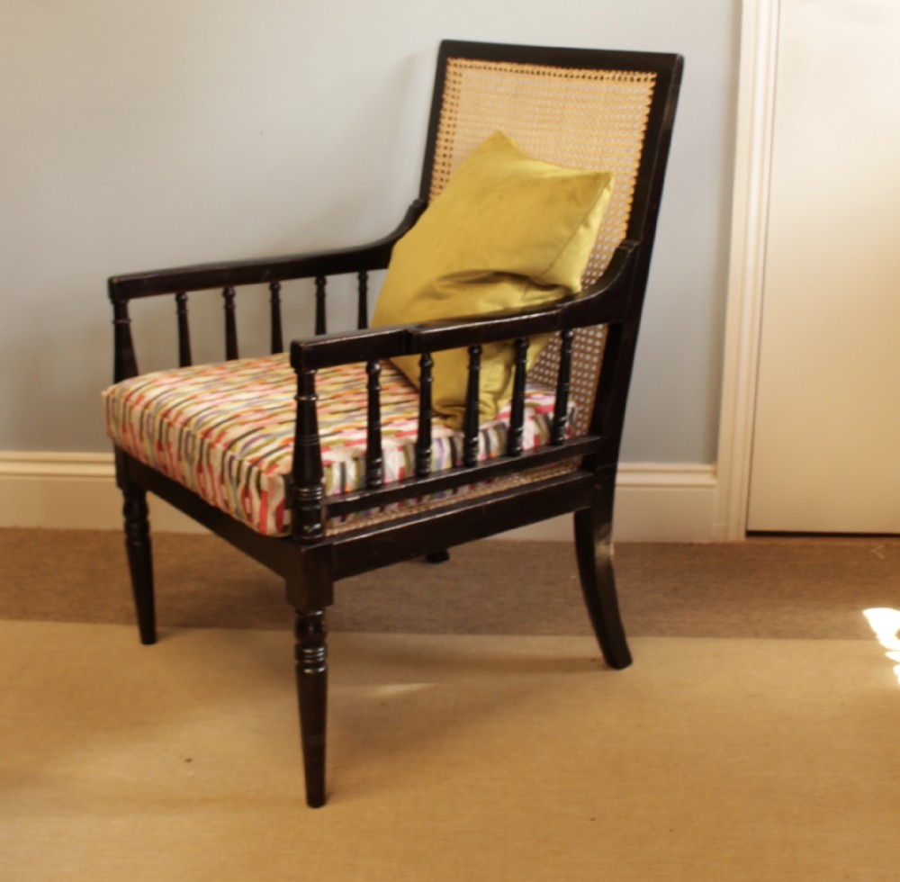 A dark wooden armchair with a woven cane backrest and spindle arm supports, featuring a patterned seat cushion.