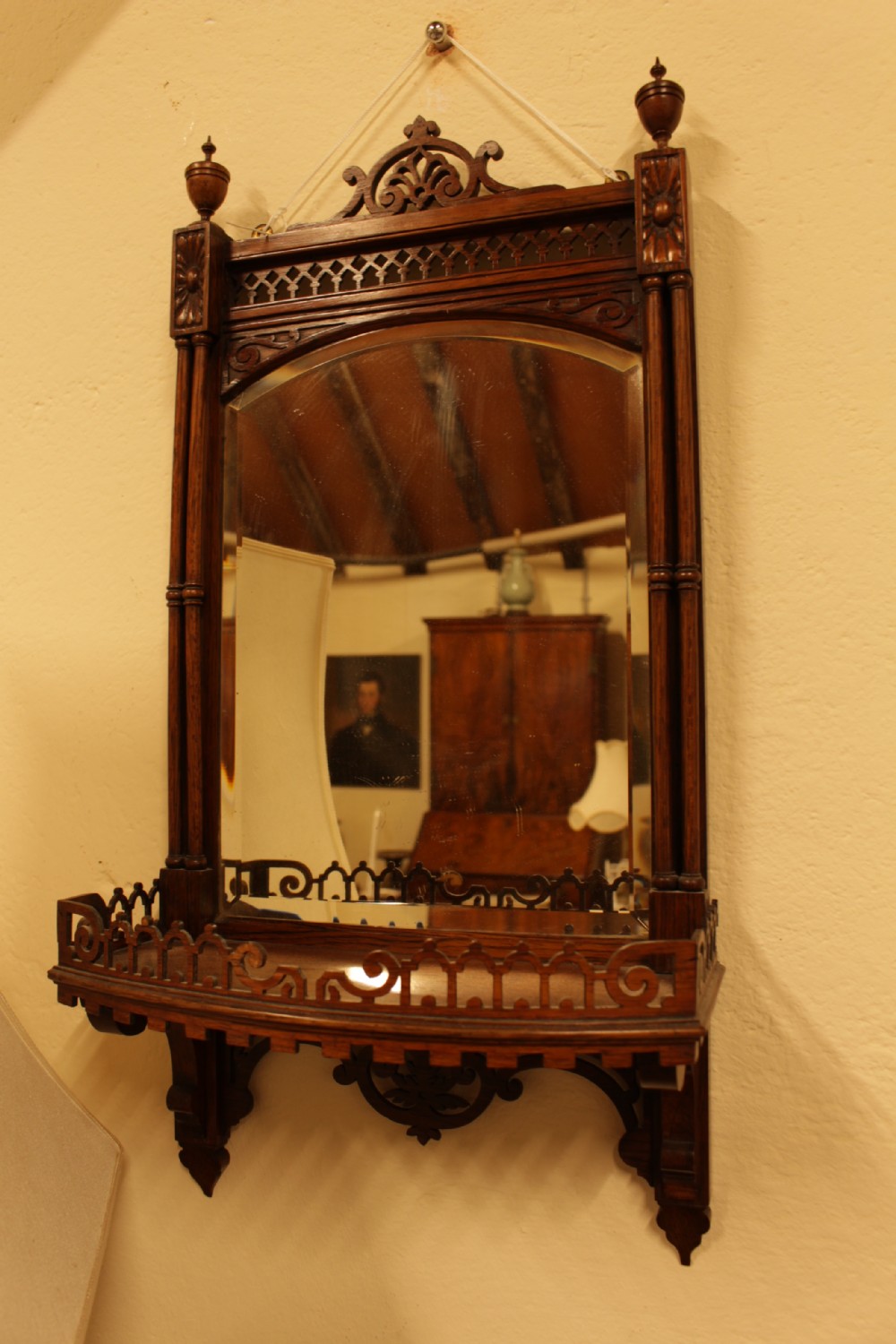 A 19th-century carved rosewood wall mirror featuring an integrated shelf with fretwork gallery, turned side columns, finials, and a bevelled mirror glass plate.