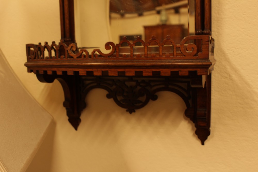 A 19th-century carved rosewood wall mirror featuring an integrated shelf with fretwork gallery, turned side columns, finials, and a bevelled mirror glass plate. View IV