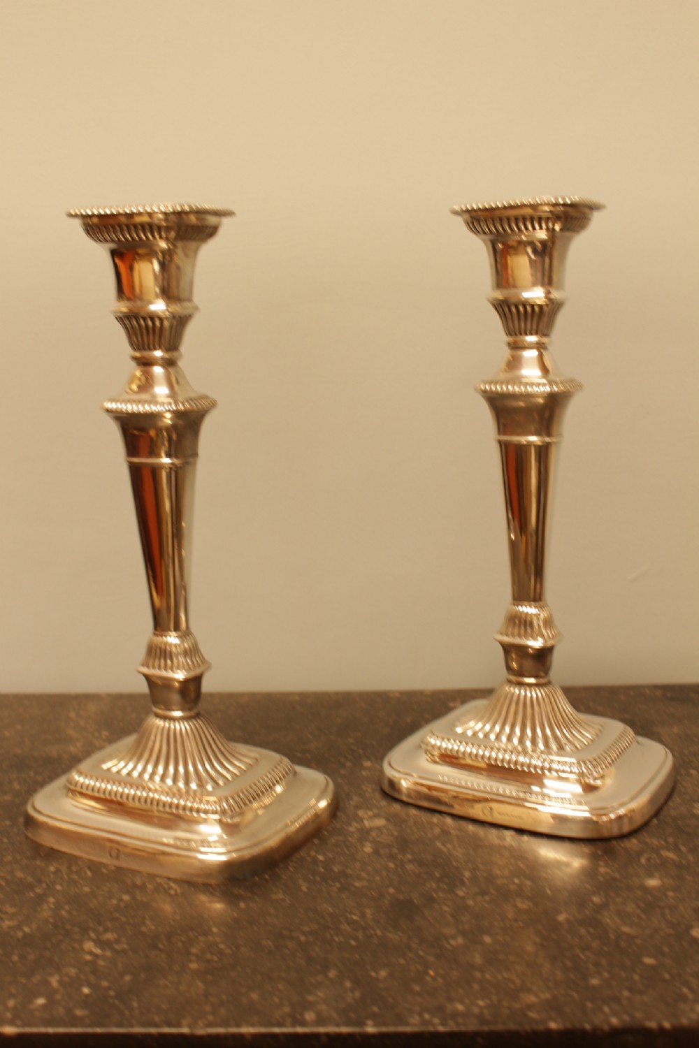 A pair of silver-plated candlesticks featuring turned fluted stems and gadrooned square bases.