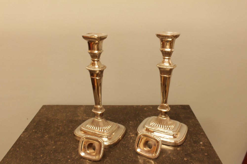 A pair of silver-plated candlesticks featuring turned fluted stems and gadrooned square bases. View V