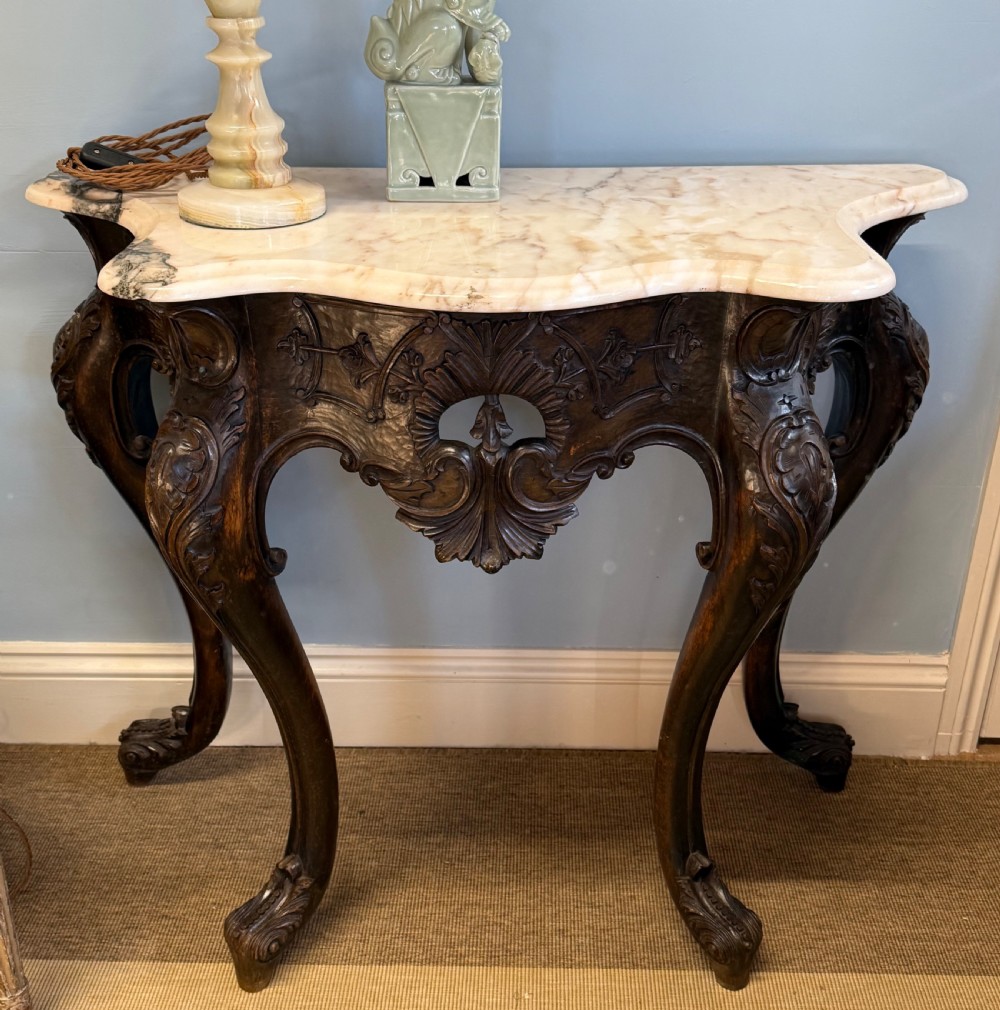A carved dark walnut Continental console table with a serpentine white marble top, cabriole legs, and an intricately carved apron featuring acanthus motifs.