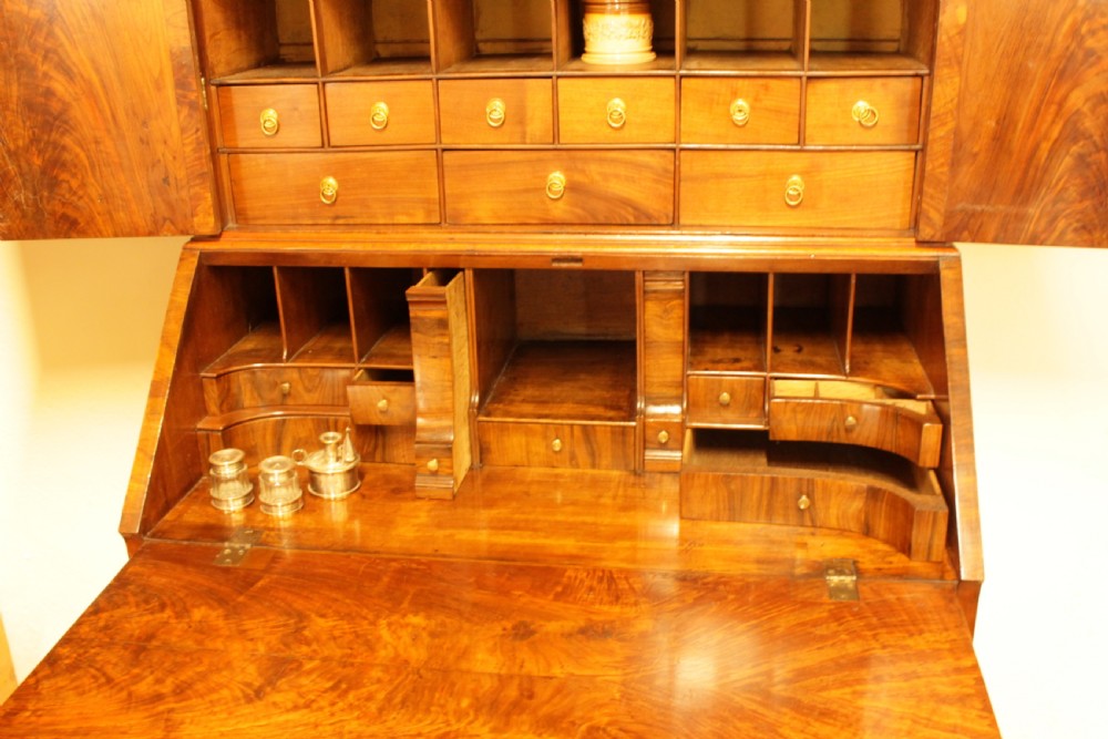 An eighteenth-century walnut bureau bookcase featuring two cupboard doors over a slant-front writing flap with four lower drawers and brass handles. View V