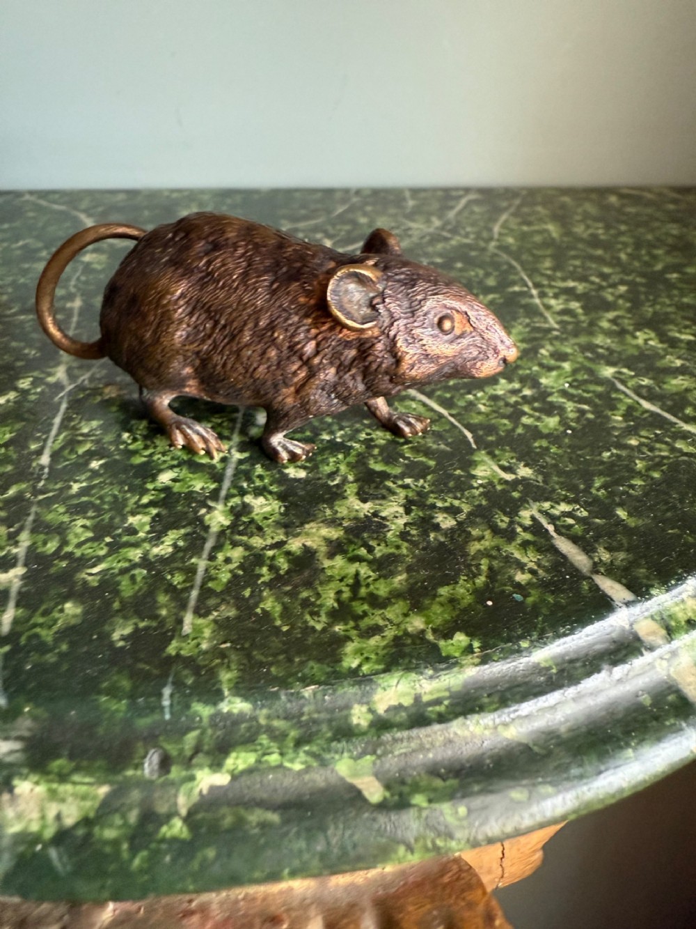 A small patinated bronze mouse figurine depicted with textured fur detailing and a thin curved tail.
