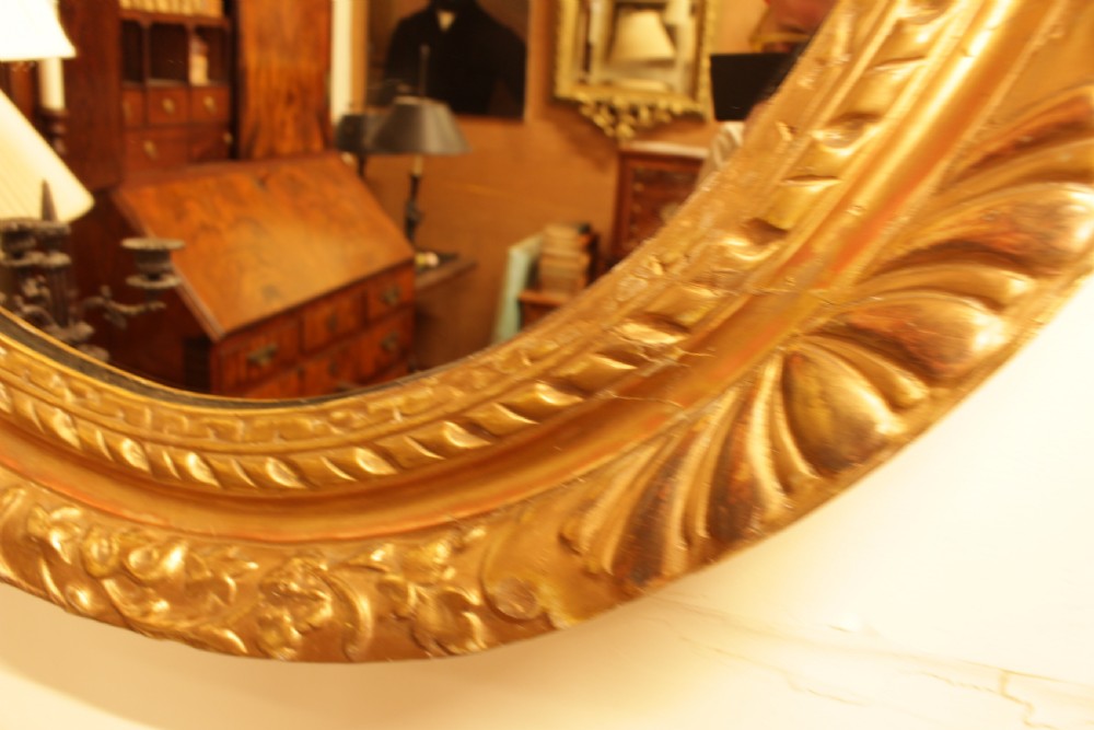A large 18th-century Georgian oval wall mirror featuring a hand-carved giltwood frame decorated with acanthus leaf motifs. View VI