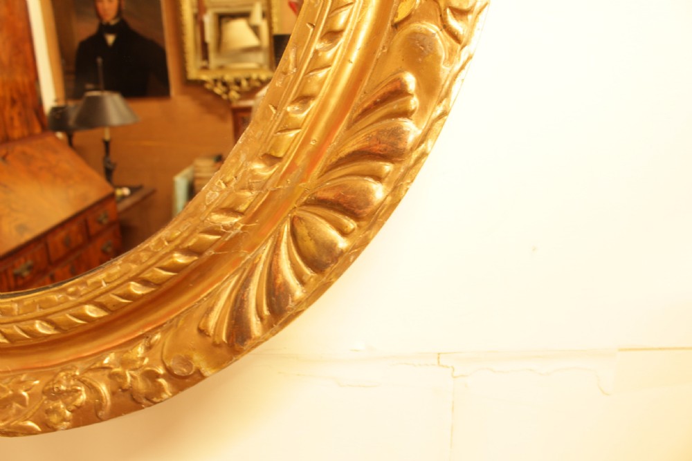 A large 18th-century Georgian oval wall mirror featuring a hand-carved giltwood frame decorated with acanthus leaf motifs. View VII