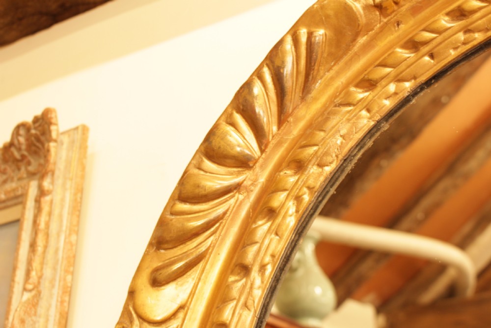 A large 18th-century Georgian oval wall mirror featuring a hand-carved giltwood frame decorated with acanthus leaf motifs. View VIII
