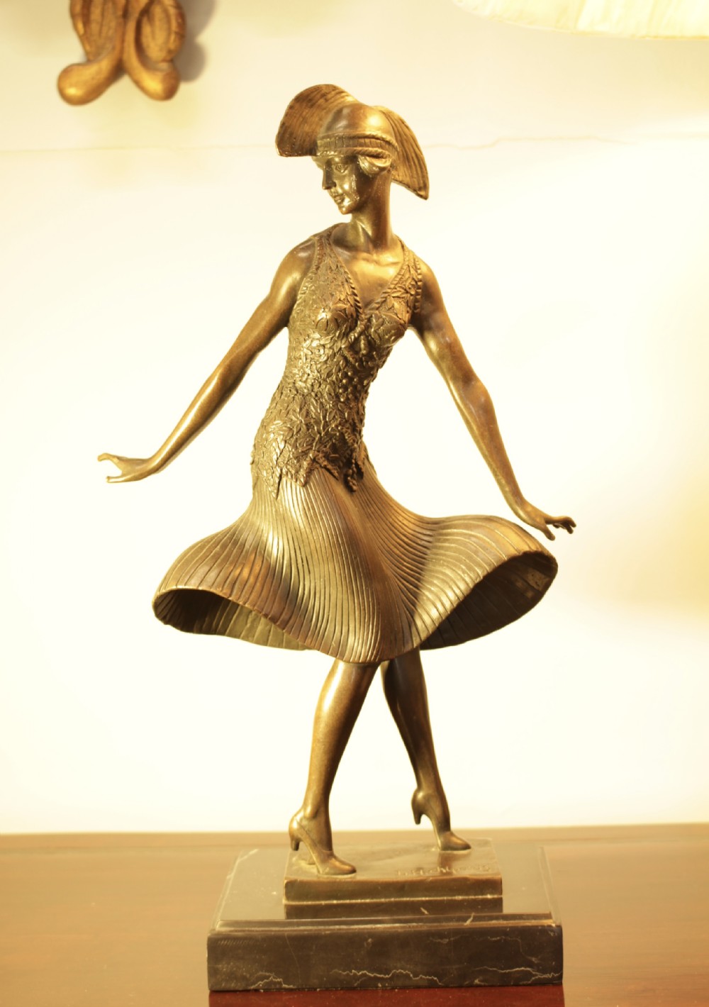 An Art Deco bronze sculpture depicting a stylized female dancer in a pleated dress and cloche headpiece mounted on a marble base.