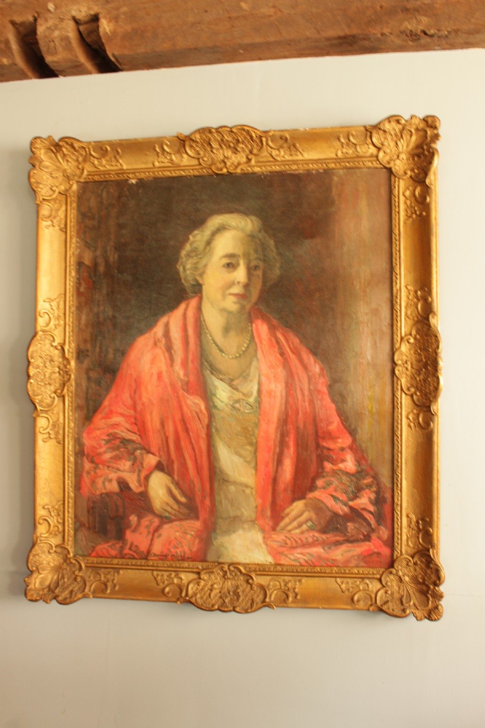 An oil painting depicting a seated woman wearing a coral shawl and a necklace, set within an ornate carved gilt frame.