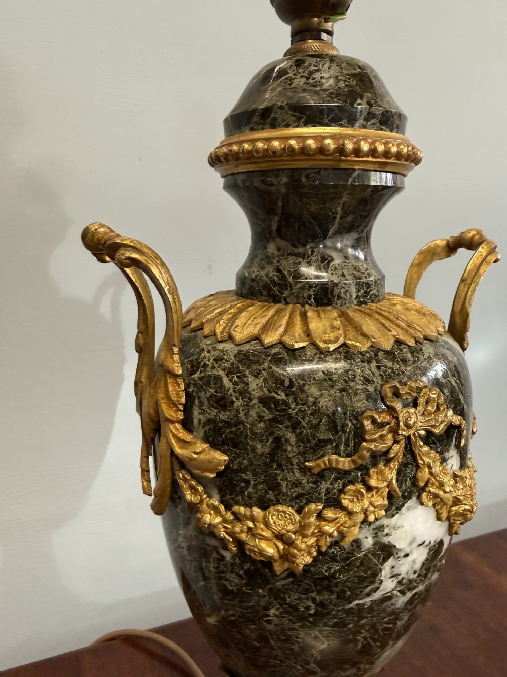 A Neoclassical style table lamp crafted from dark green veined marble in an urn form with decorative gilt metal handles and a cream pleated shade. View VI
