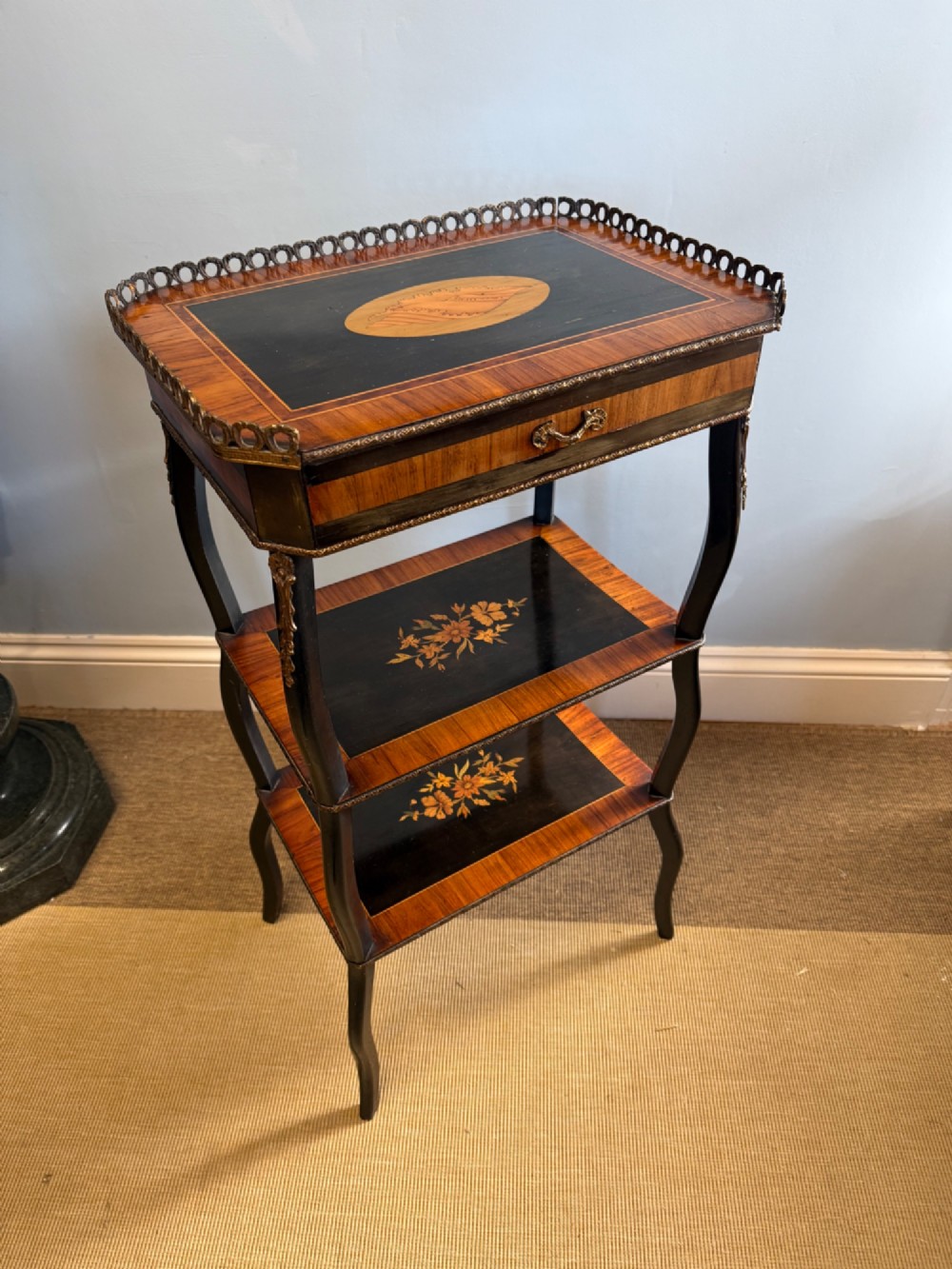 A three-tiered French ebonised walnut whatnot table with marquetry floral inlays, a single drawer, cabriole legs, and a pierced brass top gallery.
