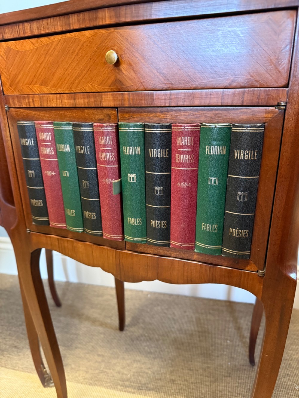 A pair of French walnut bedside tables featuring faux book spine cabinet doors, single drawers with chevron veneer patterns, and slender cabriole legs ending in brass sabots. View III