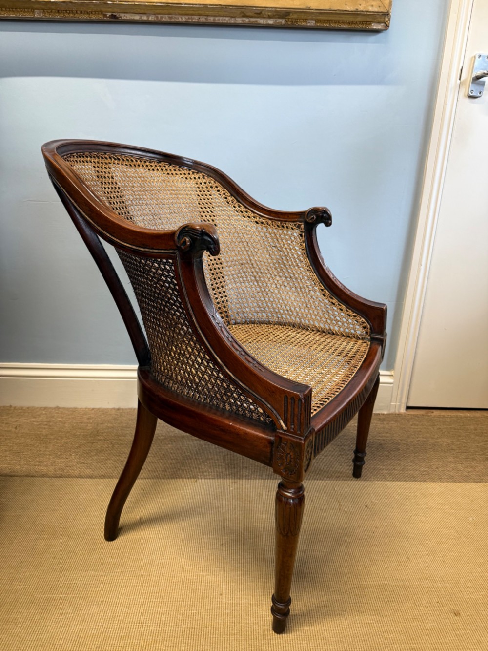 An antique mahogany bergere armchair featuring hand-woven cane panels, a curved backrest, fluted seat rail, and turned front legs. View II