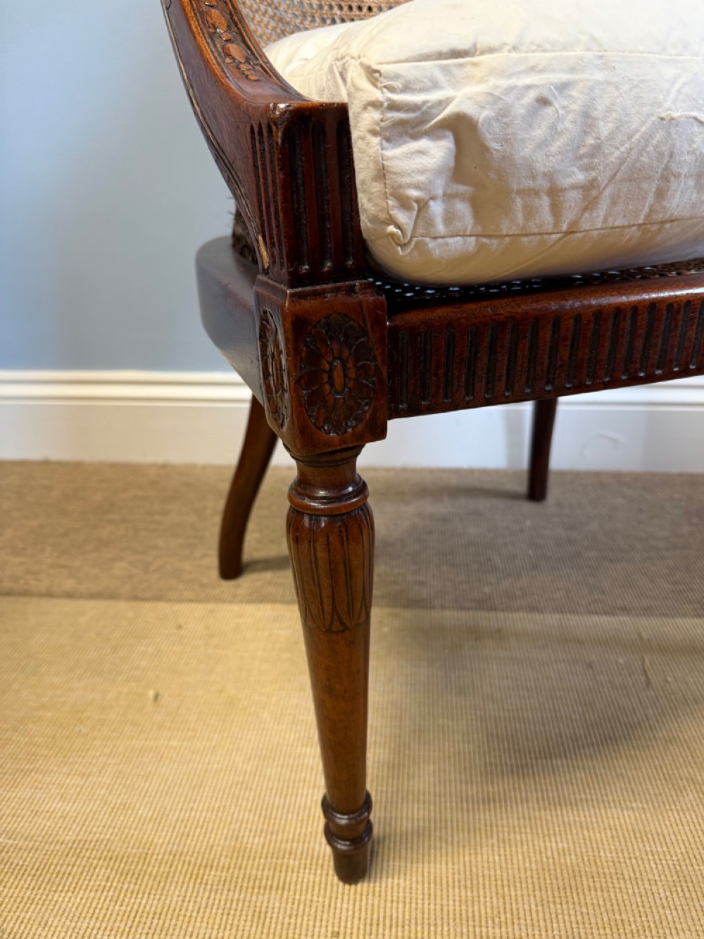 An antique mahogany bergere armchair featuring hand-woven cane panels, a curved backrest, fluted seat rail, and turned front legs. View V