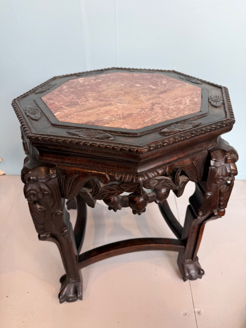 An octagonal dark carved hardwood stand featuring an inset pink marble top, openwork apron detailing, and cabriole legs.
