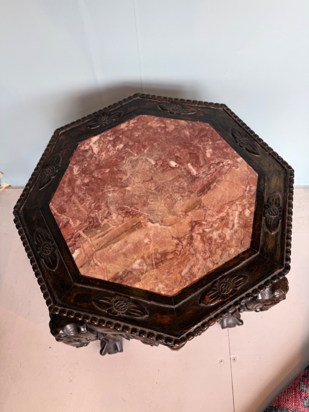 An octagonal dark carved hardwood stand featuring an inset pink marble top, openwork apron detailing, and cabriole legs. View II