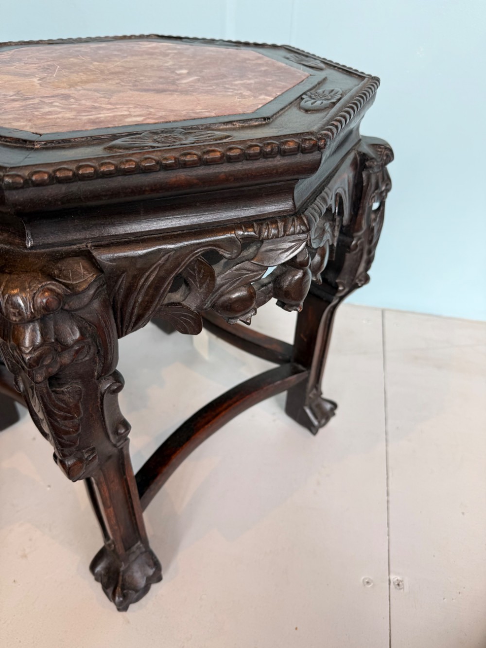 An octagonal dark carved hardwood stand featuring an inset pink marble top, openwork apron detailing, and cabriole legs. View IV