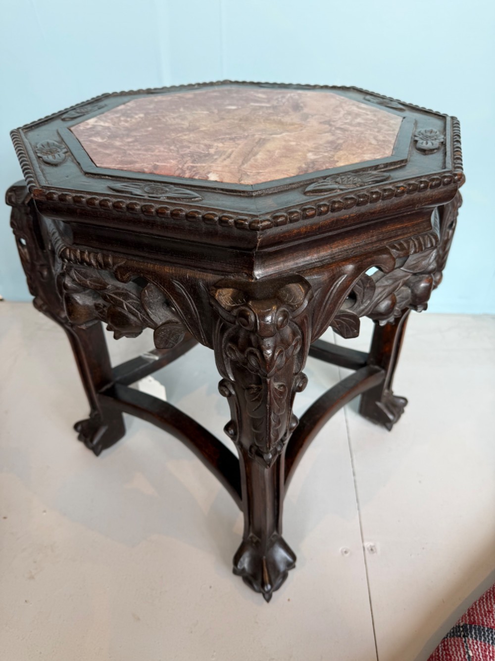 An octagonal dark carved hardwood stand featuring an inset pink marble top, openwork apron detailing, and cabriole legs. View VI