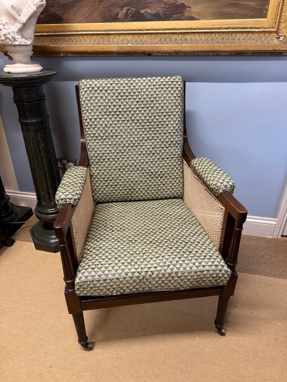 A late 19th-century mahogany bergere armchair with woven cane sides, fluted front legs on brass castors, green patterned seat cushion, and a floral upholstered backrest. View II