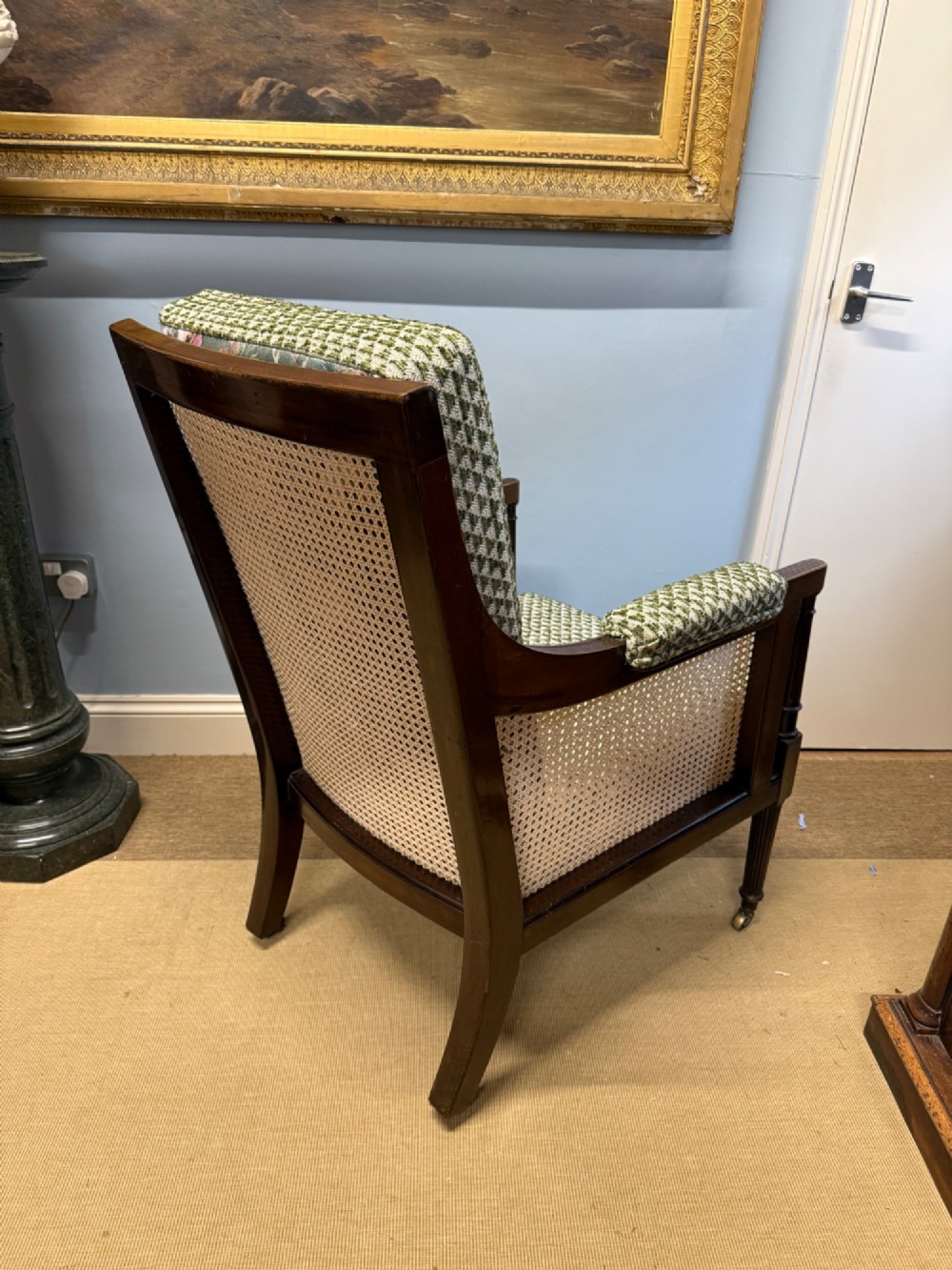 A late 19th-century mahogany bergere armchair with woven cane sides, fluted front legs on brass castors, green patterned seat cushion, and a floral upholstered backrest. View IV